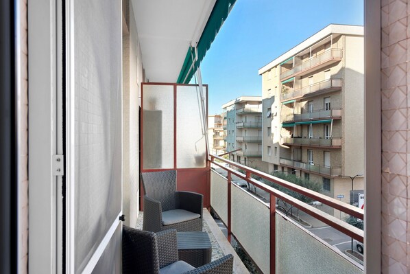 A balcony with wicker furniture, a view of adjacent buildings, and a clear sky.