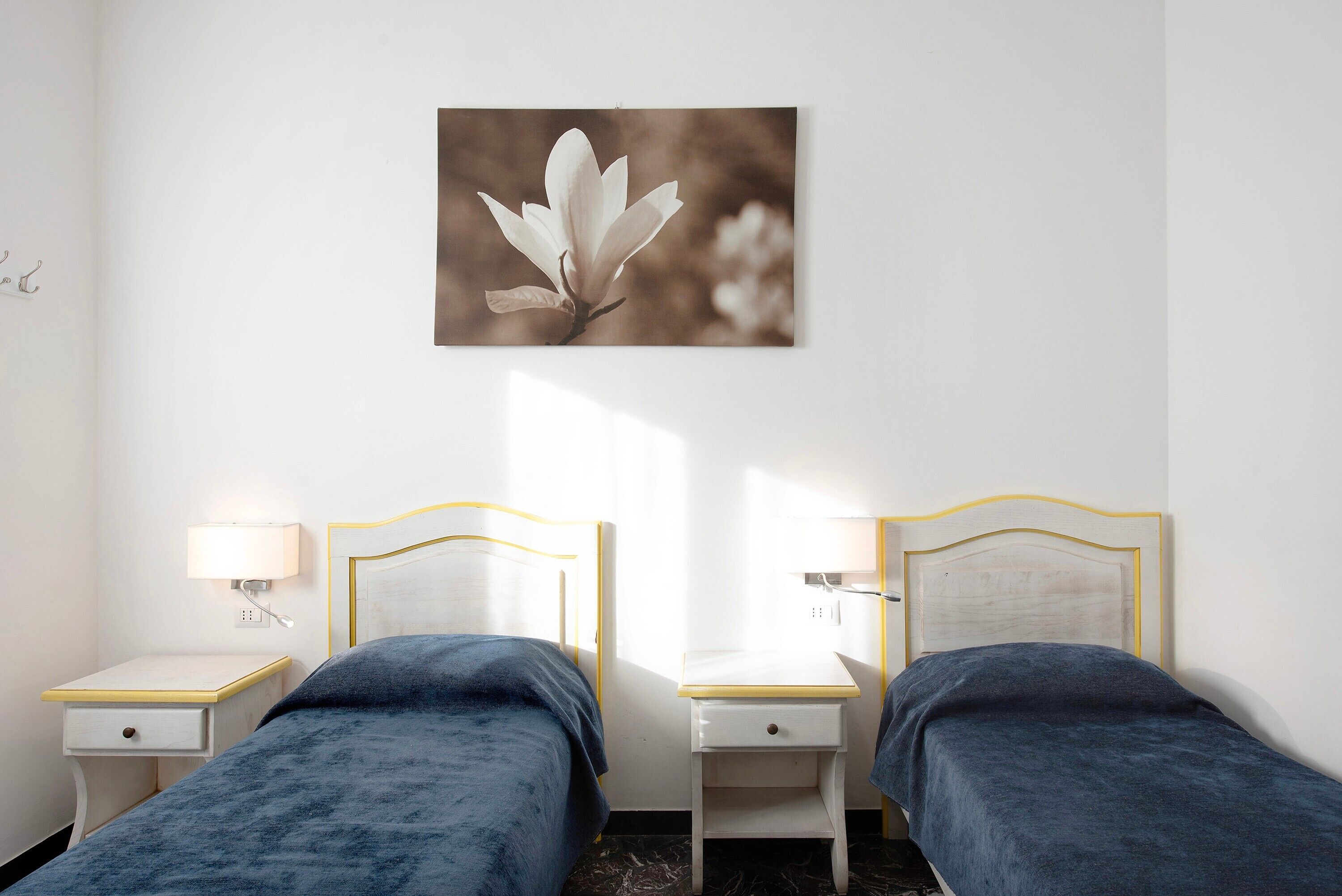 A hotel room with two beds, a bedside table with a lamp, and a wall-mounted picture.