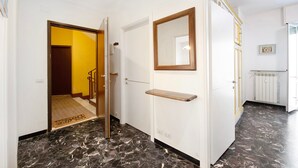 Un couloir doté d’un sol en marbre, d’une porte avec un miroir et d’un radiateur.