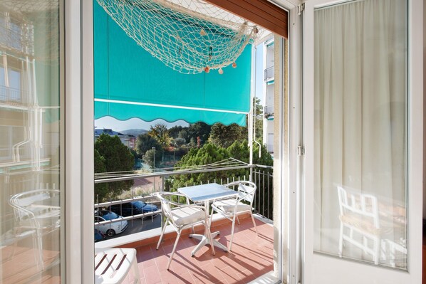 A balcony with a table and chairs, a hanging net, and a view of a road and greenery.