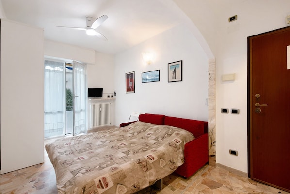 Un dormitorio con cama, un sofá rojo, un ventilador de techo y una puerta.