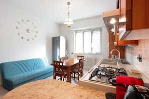 Una cocina moderna con estufa a gas, una mesa de comedor con sillas, un sofá azul y un reloj de pared.