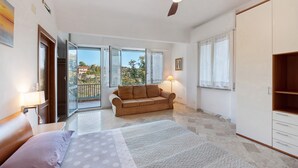 Un dormitorio con cama, sofá, ventilador de techo, armario y balcón con vistas.