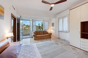 Un dormitorio con cama, sofá, ventilador de techo, armario y balc ón con vistas.
