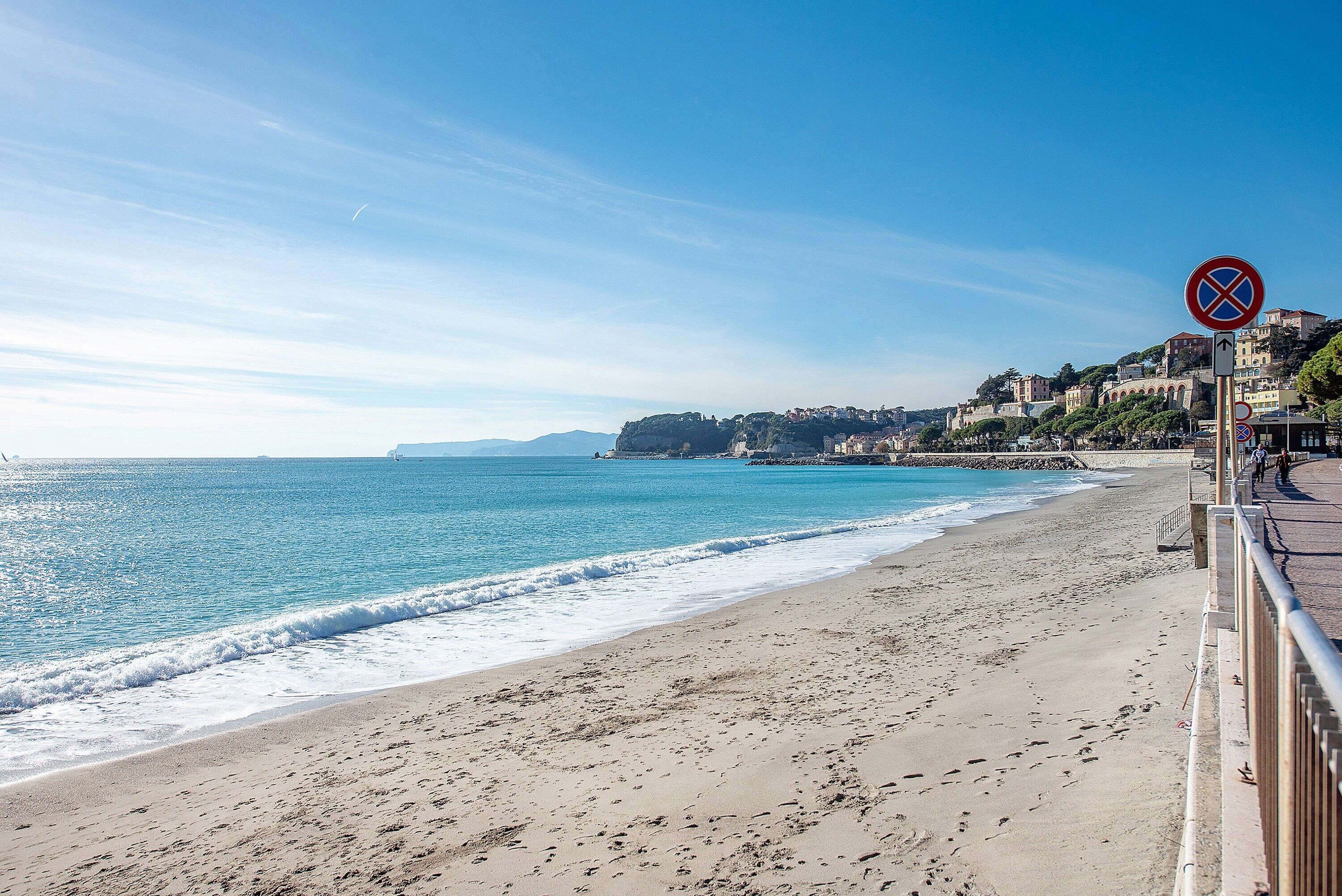 A beach with a clear sky, a no parking sign, and buildings along the coastline.