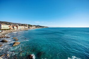 Une ville côtière avec des bâtiments qui bordent la plage, une eau d’un bleu limpide et un littoral rocheux.