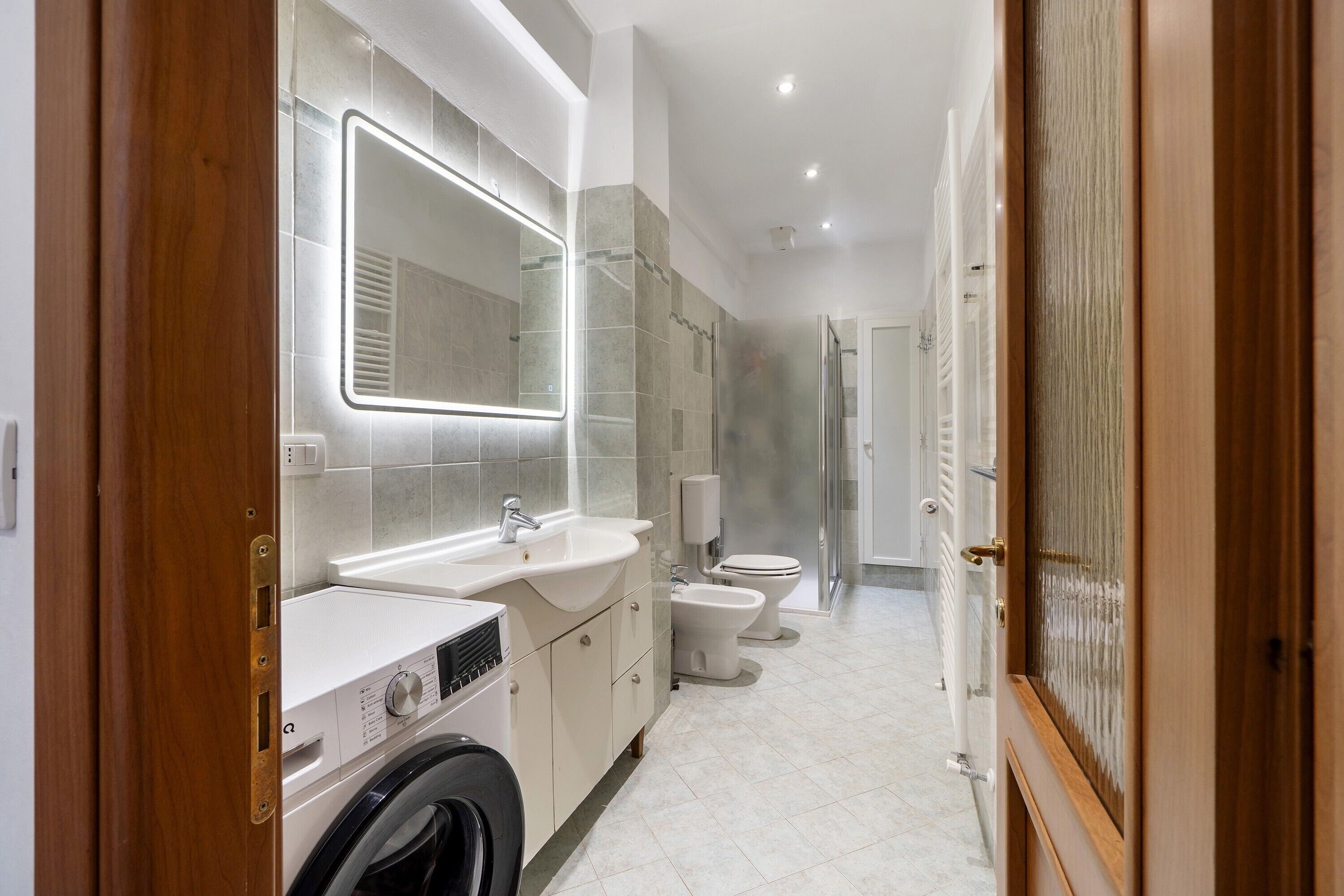 Un bany modern amb rentadora, un mirall gran, un lavabo i un vàter.