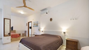 Une chambre à coucher comprenant un lit, un bureau, une chaise, une commode et un ventilateur de plafond.