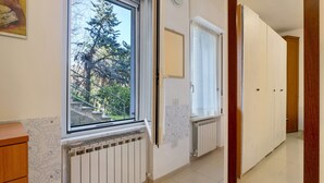 Une pièce dotée d’une grande fenêtre, d’un radiateur, d’une armoire en bois et d’une porte donnant sur une autre pièce.