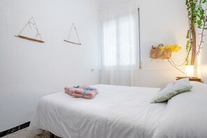 A neatly made bed with folded towels, a bedside table with a lamp, and a window with sheer curtains.