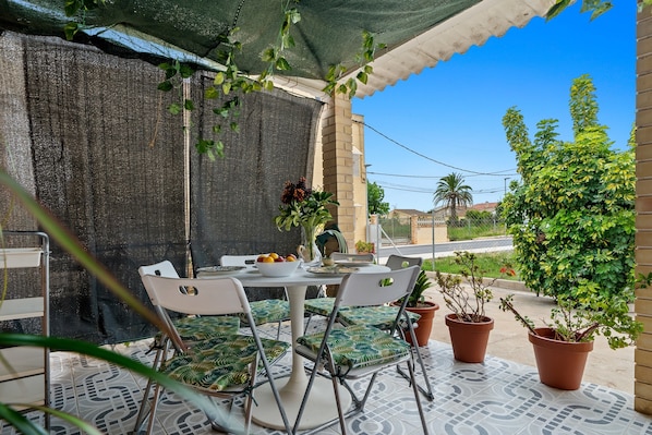 An outdoor patio with a table and chairs, potted plants, and a covered area.