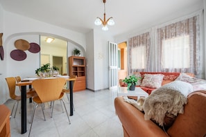 A modern living room with a dining area, a sofa, and a chandelier.