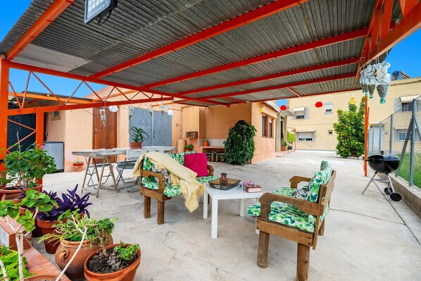 An outdoor patio with wooden furniture, potted plants, and a barbecue grill.