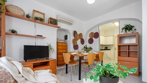 Una sala de estar moderna con un televisor de pantalla plana, estanterías de madera, una mesa de comedor con sillas y una planta en maceta.