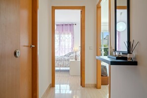 Um corredor leva a um quarto com uma cama, mesa de cabeceira e abajur.