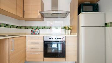 Cucina con mobili in legno, cappa in acciaio inossidabile, forno integrato, microonde e frigorifero.