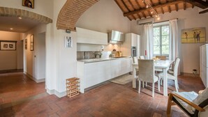 A spacious kitchen with white cabinetry, a brick archway, and a dining area with white chairs and a table. - Holiday Home 'Beretone' with Mountain View, Wi-Fi and Air Conditioning (Radda In Chianti)
