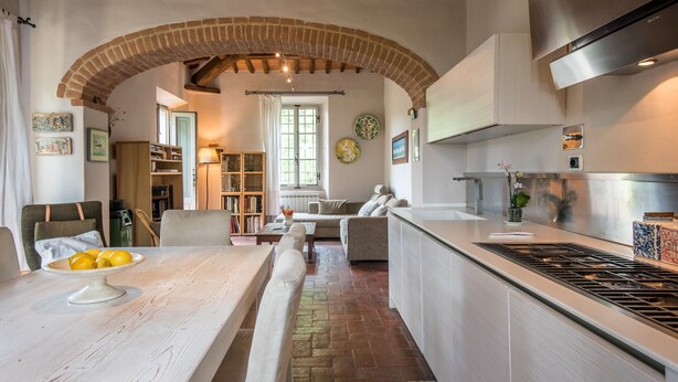 A kitchen with a brick archway, a dining area with a table and chairs, and a living room with a sofa. - Holiday Home 'Beretone' with Mountain View, Wi-Fi and Air Conditioning (Radda In Chianti)