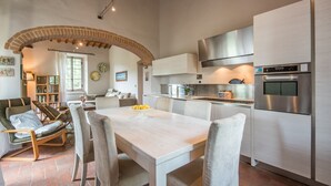 A modern kitchen with a dining area, featuring a brick archway, stainless steel appliances, and a light-colored wooden table. - Holiday Home 'Beretone' with Mountain View, Wi-Fi and Air Conditioning (Radda In Chianti)