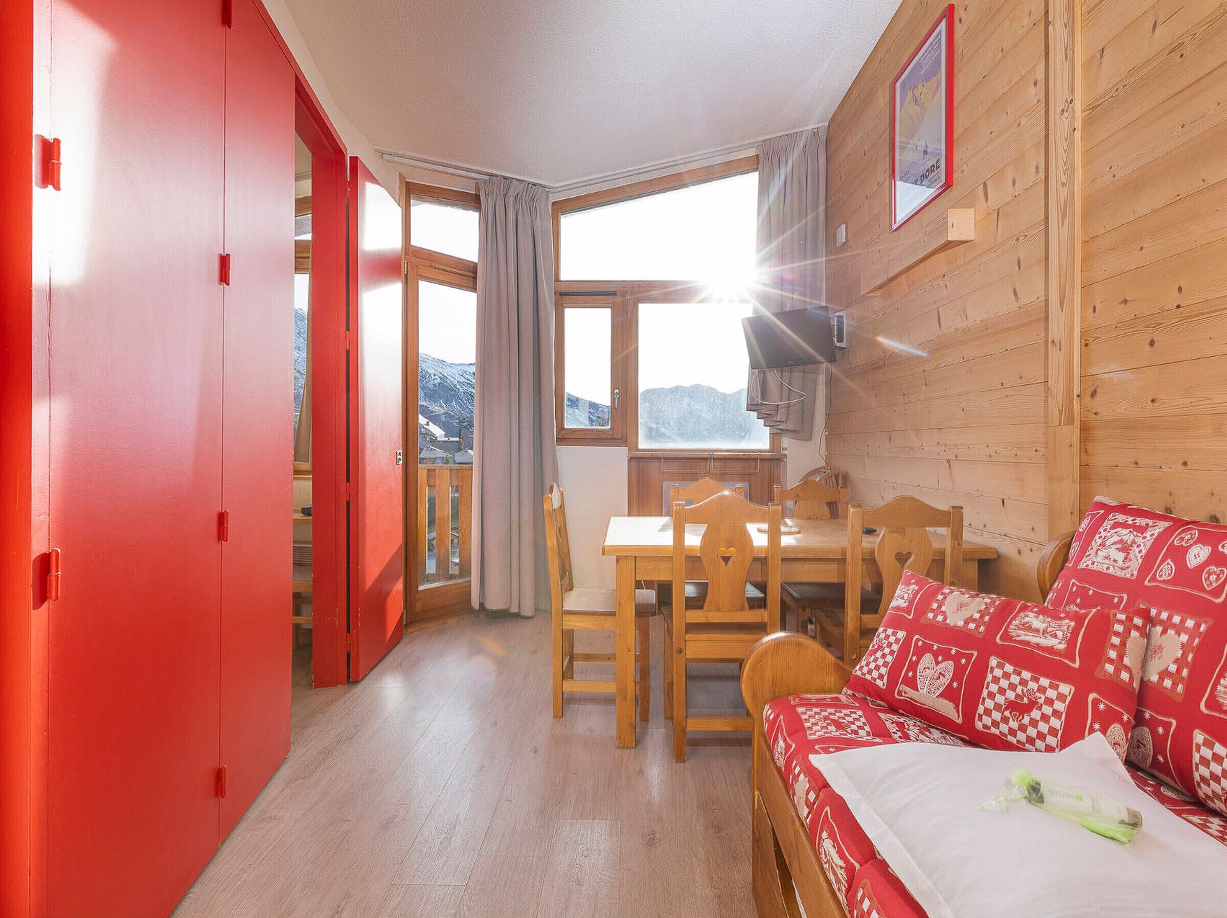 A cozy room with a wooden table, chairs, and a red sofa with patterned cushions.