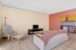 A living room with a sofa, a chair, a TV, and a kitchen area in the background. - Holiday Home 'Casa Sirius' with Sea View, Private Terrace and Wi-Fi (Tijarafe)