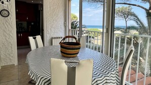 Un coin repas avec une table dressée pour deux personnes, un panier en osier et une vue sur la mer depuis un balcon.