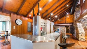 Een keuken met een centraal eiland, houten balken in het plafond, stenen muren en een klok aan de muur.