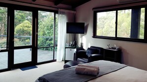 Een slaapkamer met een bed, een televisie, een stoel en een raam met uitzicht op bomen.