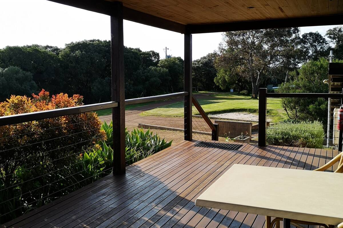 Een houten terras met een tafel en stoelen, met uitzicht op een verzorgd gazon en bomen.