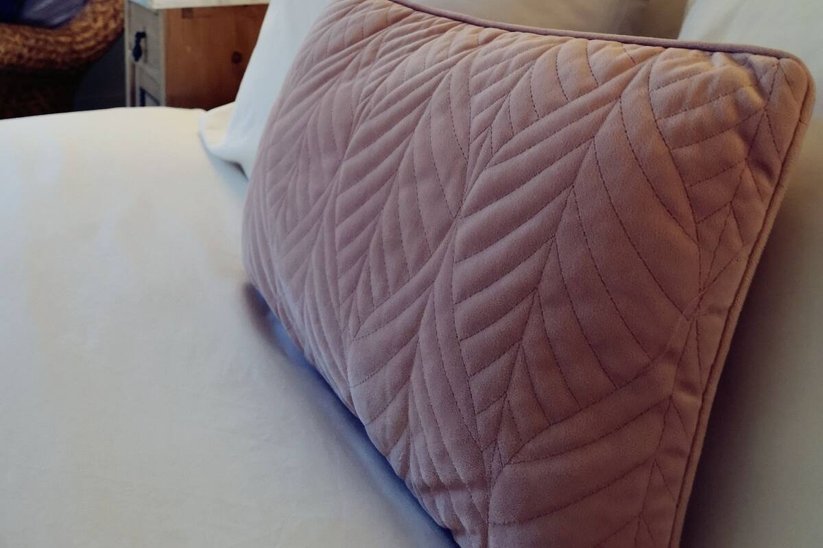 Een net opgemaakt bed met een gebogen kussen en een bedlampje.