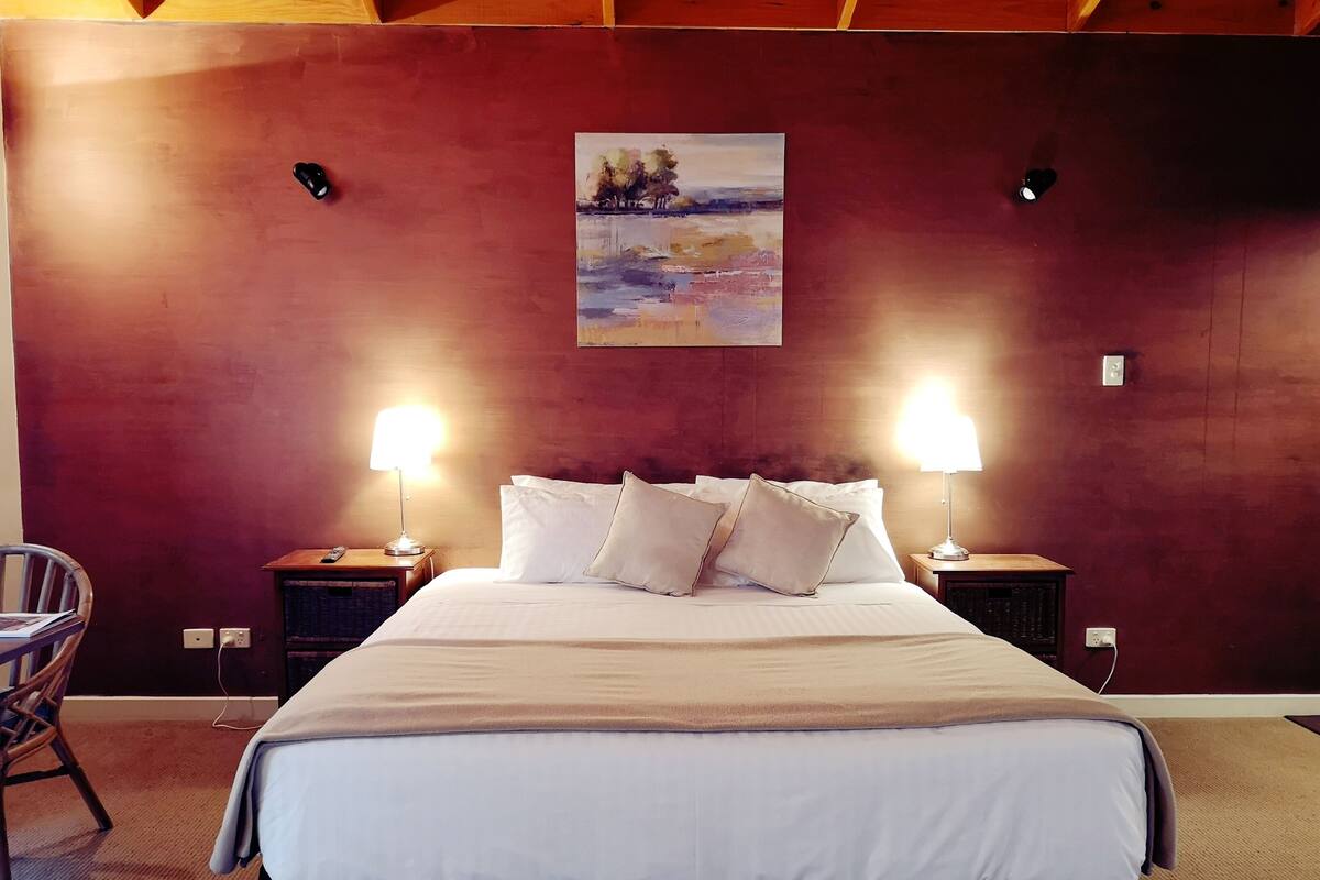 Een hotelkamer met een groot bed, twee bedlampen, een schilderij aan de muur en een stoel.