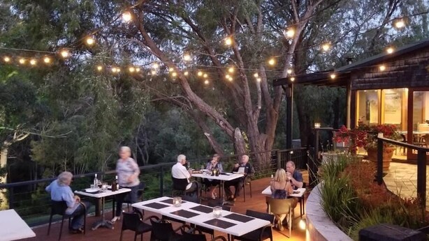 Een terras met tafels en stoelen, sfeerverlichting en een gebouw met grote ramen.