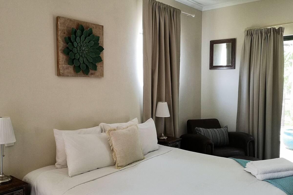 Een hotelkamer met een groot bed, een bureau met een lamp, een stoel en een spiegel aan de muur.