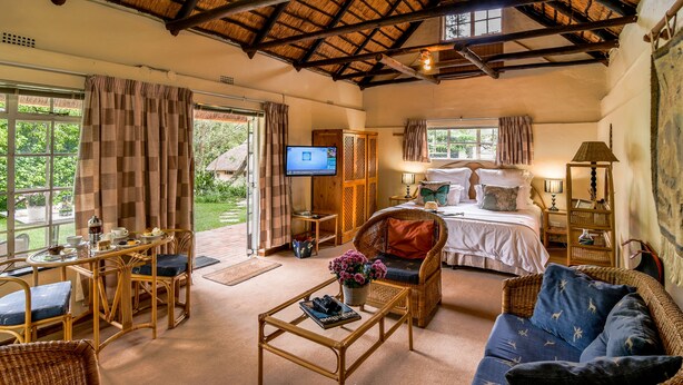 A spacious room with a bed, a television, a dining area, and a seating area with a coffee table and chairs.