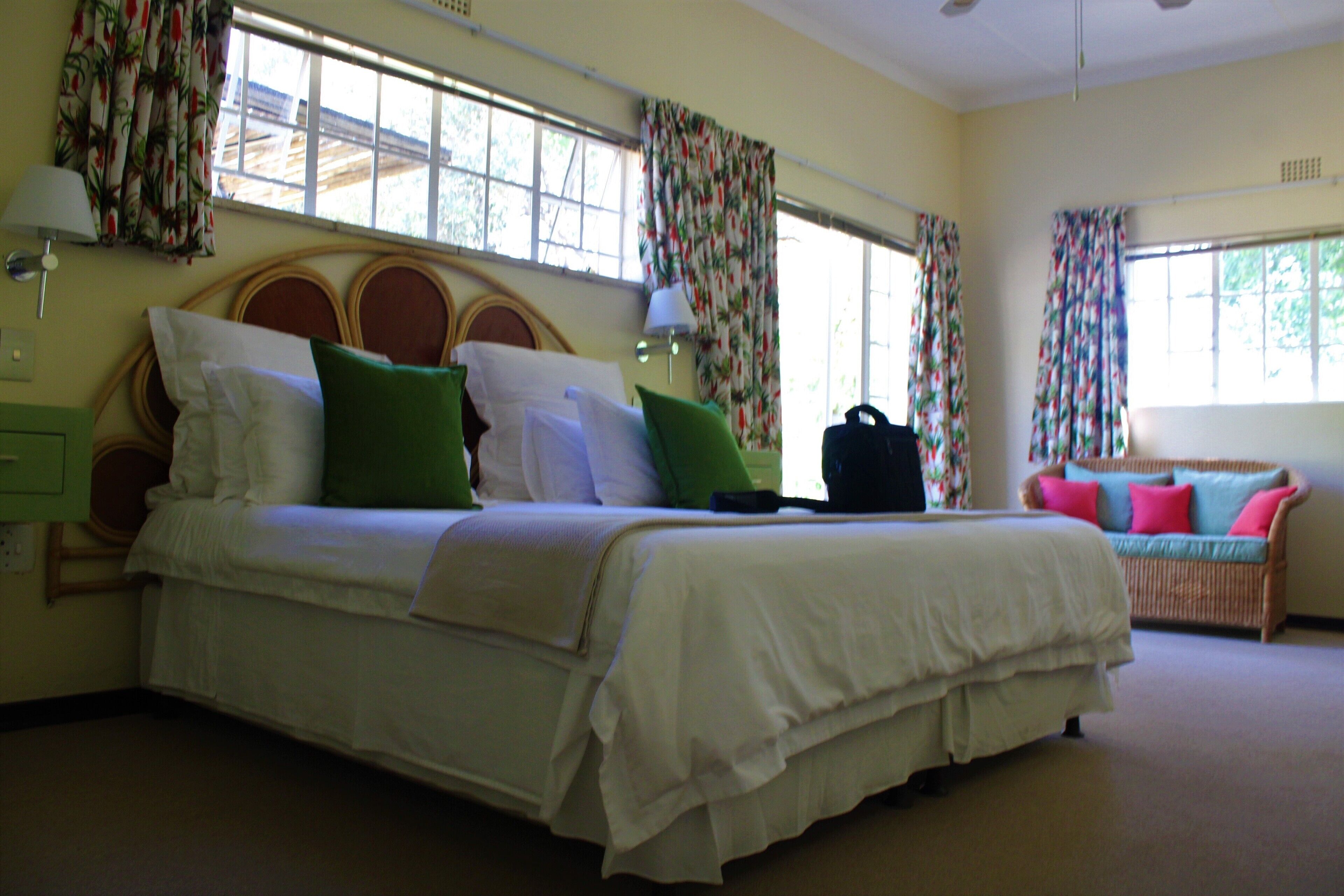 A bedroom with a large bed, a wicker sofa, and a window with curtains.