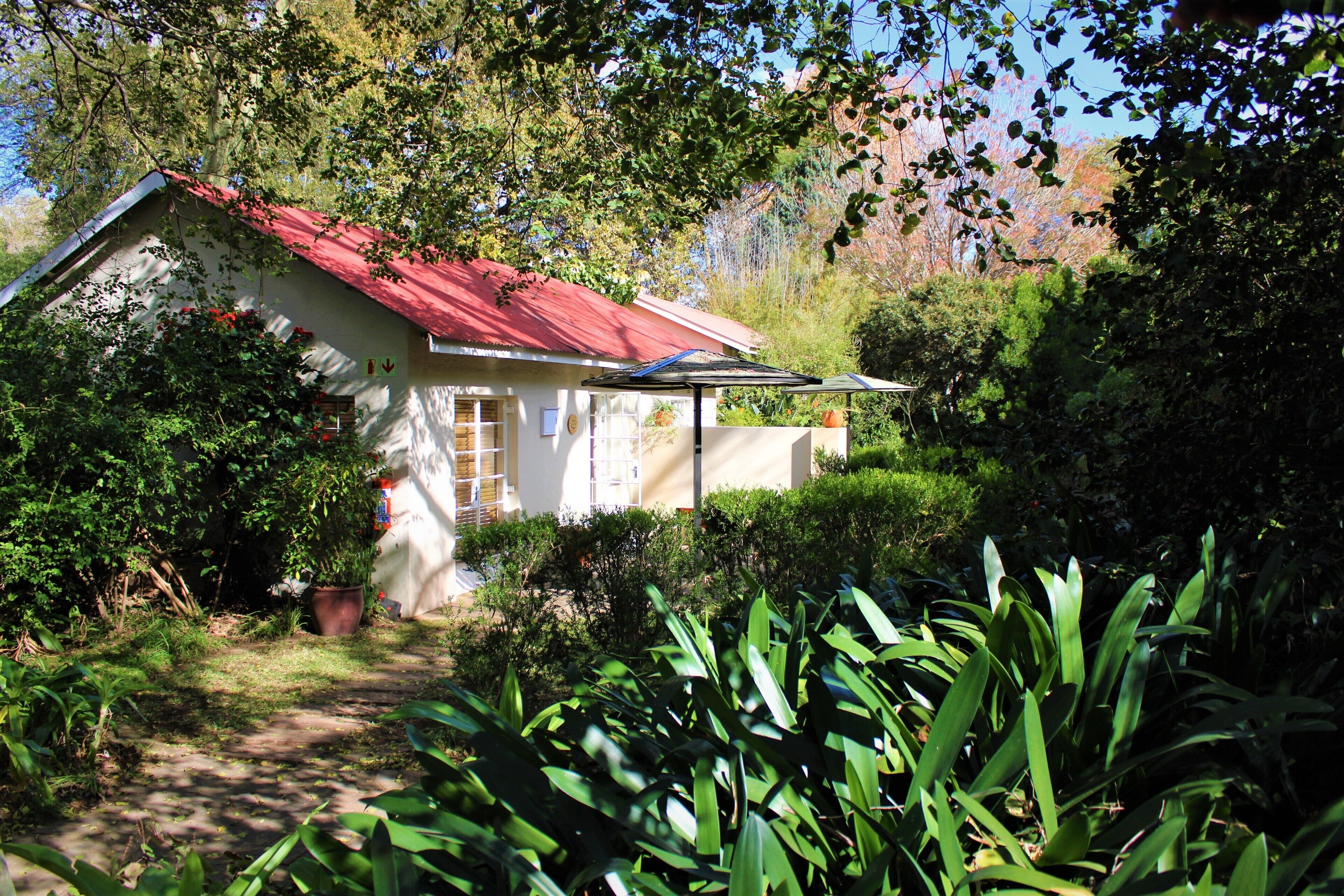 A small house with a red roof, surrounded by lush greenery and trees.