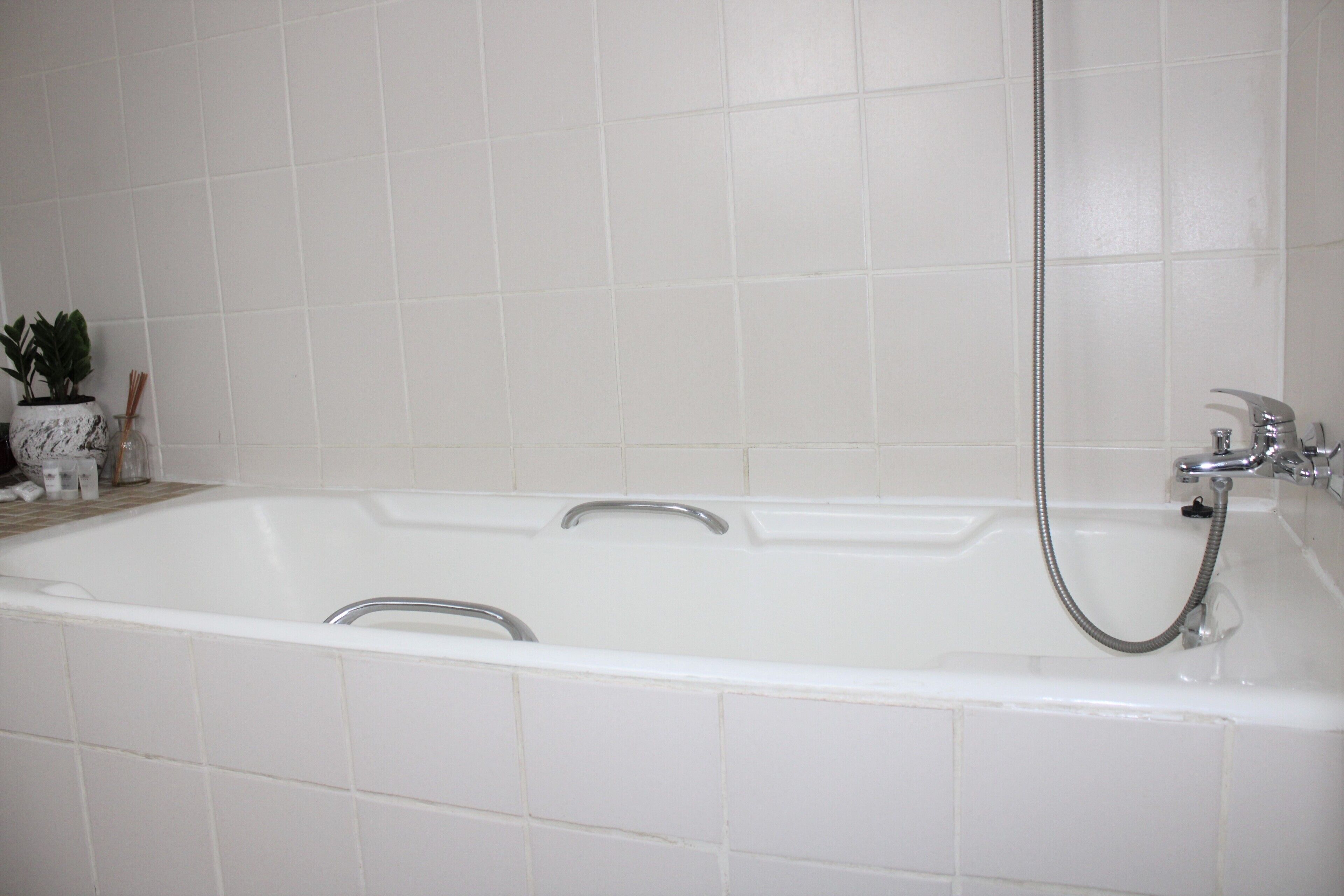 A white bathtub with a shower head and faucet, set against a tiled wall.