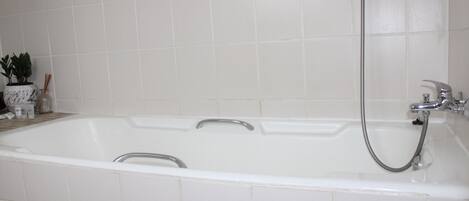 A white bathtub with a shower head and faucet, set against a tiled wall.