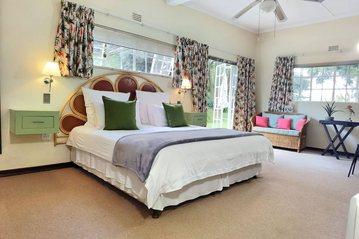A bedroom with a large bed, a green nightstand, a wicker sofa, and a small table with a potted plant.