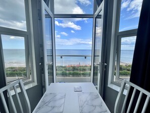 Een balkon met uitzicht op zee en strand, een witte tafel met marmeren blad en witte stoelen.
