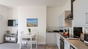 A modern kitchen with white cabinets, a dining area with a table and chairs, and a view of the beach through a window. - 2 Seaview @ Bridlington Bay (Bridlington)
