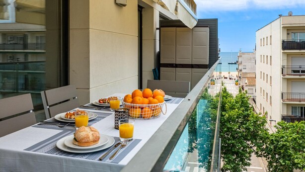 A balcony with a table set for breakfast, including orange juice and a basket of oranges.