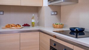 A modern kitchen with wooden cabinets, a built-in stove, and a countertop with food items like bread, grapes, and a bottle of wine.