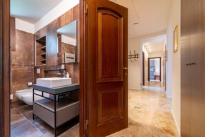 A modern bathroom with a large mirror, a sink, and a toilet. There is a wooden door leading to a hallway with a coat rack and a mirror. - Eleganza e Stile nel Cuore di Bellagio by Wonderful Italy (Bellagio)