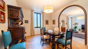 A dining area with a wooden table and chairs, a chandelier, and a view through an archway to another room.