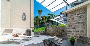 An outdoor patio with lounge chairs, a dining table with chairs, and a stone wall. - Eleganza e Stile nel Cuore di Bellagio by Wonderful Italy (Bellagio)