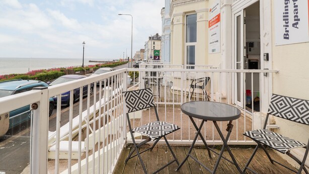 A balcony with a view of the sea, a table, and two chairs.