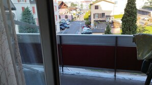 Blick von einem Balkon mit Geländer auf eine Straße mit parkenden Autos und Gebäuden.