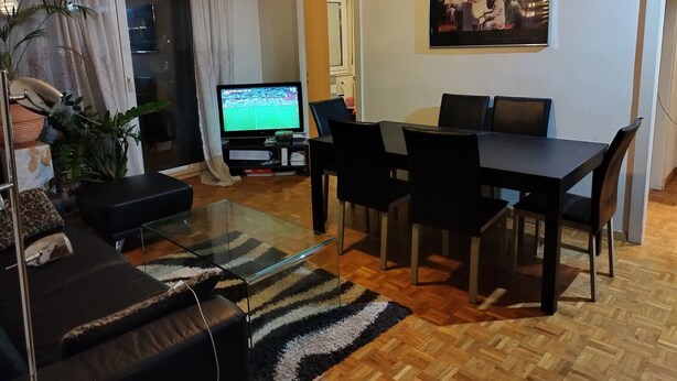 Ein Wohnzimmer mit Fernseher, einer Couch, einem Couchtisch und einem Essbereich mit Stühlen.