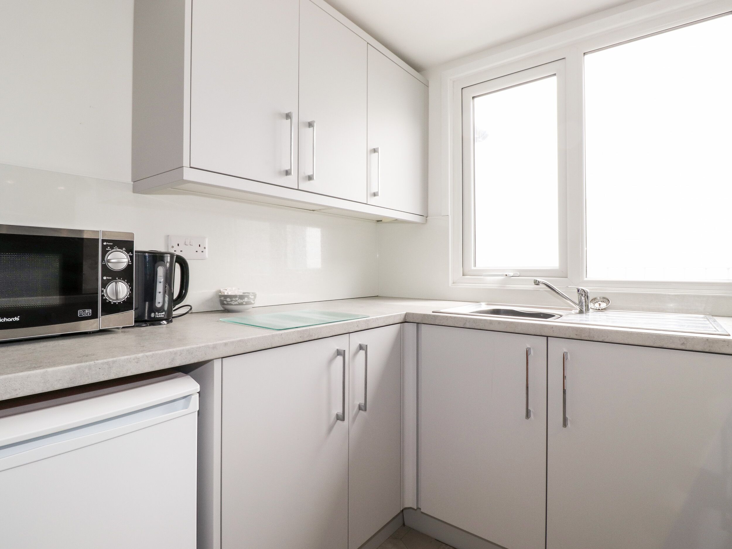A modern kitchen with white cabinets, a black microwave, a coffee maker, and a window providing natural light.